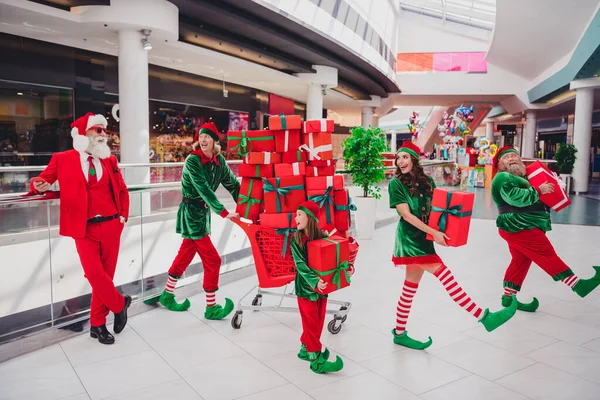 Ritratto di attraenti alla moda allegri amici elfi che trasportano scatole regalo vigilia tempo affare divertirsi al centro commerciale al chiuso — Foto Stock