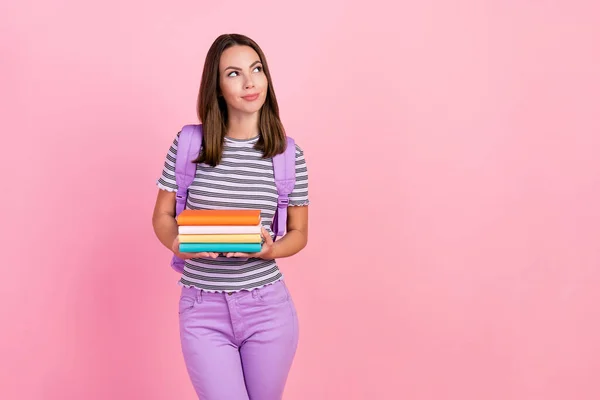 Фото чарівної мрійливої молодої леді носить смугастий рюкзак, посміхаючись тримаючи копії книг, які виглядають порожнім простором ізольований рожевий колір фону — стокове фото