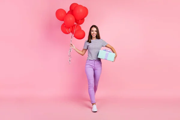 Φωτογραφία από αξιολάτρευτο λαμπερό νεαρή γυναίκα ντυμένος ριγέ ρούχα κρατώντας πολλά κόκκινα μπαλόνια δώρο κουτί χαμογελώντας απομονωμένο ροζ χρώμα φόντο — Φωτογραφία Αρχείου