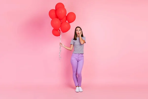 Φωτογραφία από ελκυστική εντυπωσιασμένος νεαρή γυναίκα ντυμένος ριγέ ρούχα κρατώντας πολλά κόκκινα μπαλόνια μάγουλο βραχίονα απομονωμένο ροζ χρώμα φόντο — Φωτογραφία Αρχείου