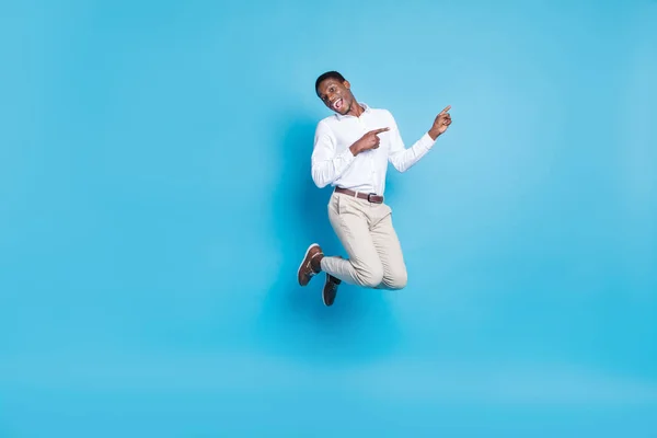 Foto de homem de pele escura funky positivo usar camisa branca sorrindo salto alto apontando espaço vazio isolado fundo de cor azul — Fotografia de Stock