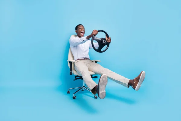 Foto de homem de pele escura funky doce usar camisa branca sorrindo cadeira sentada segurando volante isolado fundo de cor azul — Fotografia de Stock