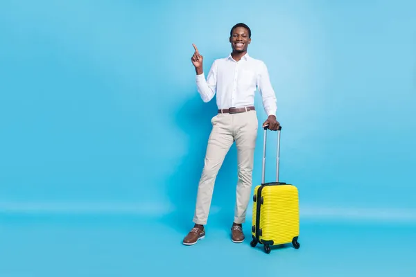 Φωτογραφία από αστείο γλυκό σκούρο δέρμα άνθρωπος φορούν λευκό πουκάμισο χαμογελώντας κρατώντας αποσκευές δείχνοντας κενό χώρο απομονωμένο φόντο μπλε χρώμα — Φωτογραφία Αρχείου
