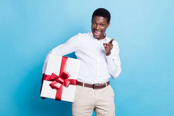 Fotografie atraktivní tmavé kůže muž nosit bílou košili s úsměvem drží velký dárek box ukazující vám izolované modré barvy pozadí — Stock fotografie