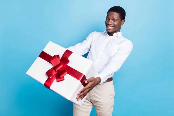Fotografie sladké atraktivní tmavé kůže muž nosit bílou košili s úsměvem drží velký dárek box izolované modré barvy pozadí — Stock fotografie
