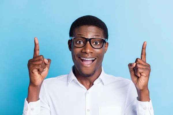 Foto de engraçado impressionado homem pele escura usar óculos de camisa branca apontando espaço vazio sorrindo isolado fundo de cor azul — Fotografia de Stock