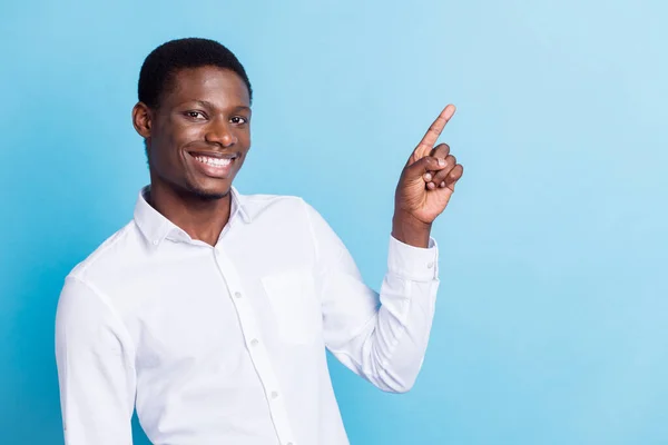 Foto de dulce atractivo chico de piel oscura vestido camisa formal sonriendo apuntando espacio vacío aislado color azul fondo —  Fotos de Stock