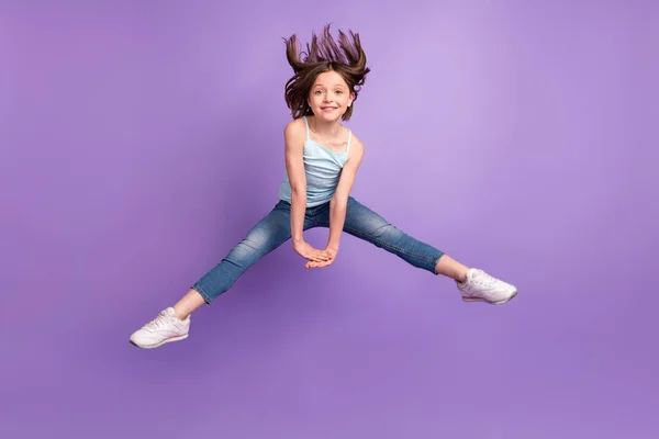 Full storlek foto av funky brun frisyr liten flicka hoppa håll händerna bära blå topp jeans isolerad på violett färg bakgrund — Stockfoto