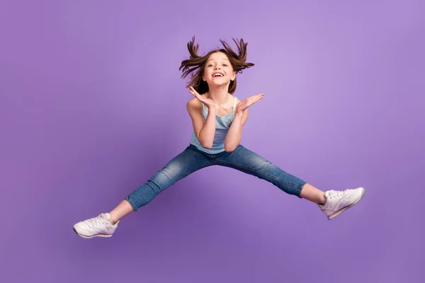 Full längd foto av roliga brun frisyr liten flicka hoppa bära blå topp jeans isolerad på violett färg bakgrund — Stockfoto