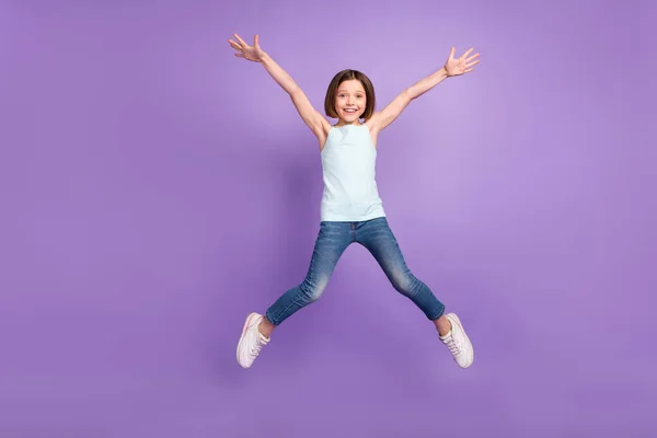 Foto de corpo inteiro de penteado marrom ativo pequena menina salto desgaste azul top jeans isolado no fundo cor violeta — Fotografia de Stock