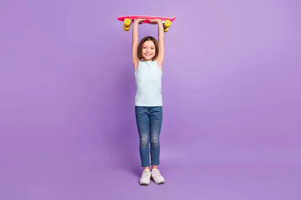 Full tělo fotografie atraktivní šťastný sportovní holčička zvýšit longboard nad hlavou izolované na fialové barevné pozadí — Stock fotografie