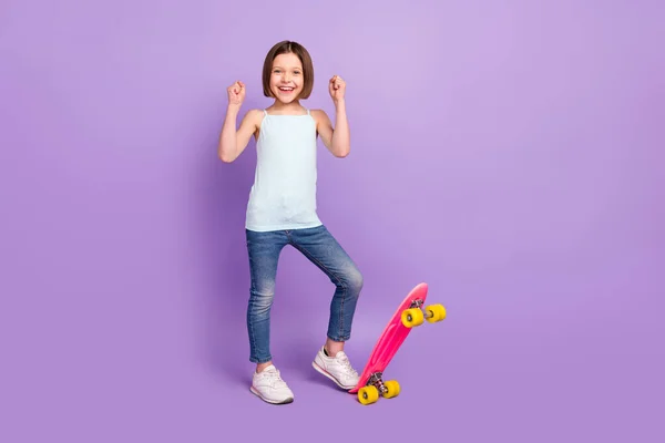 Foto de cuerpo completo de alegre feliz niña pequeña agradable levantar puños patinador ganador aislado sobre fondo de color púrpura — Foto de Stock