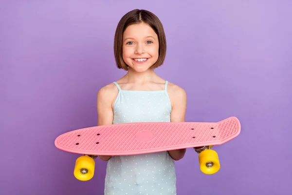 Fotografie veselý šťastný pěkný malý dívka dobrá nálada držet ruce longboard úsměv izolované na fialové barvy pozadí — Stock fotografie