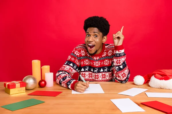 Фото молодого впечатленного брюнет парень сидеть написать точку износа праздничный свитер изолирован на красном фоне — стоковое фото