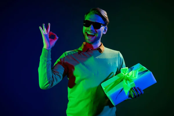 Фото молодого крутого парня тысячелетия провести настоящее шоу Оки носить очки свитер изолирован на темно-синем фоне цвета — стоковое фото