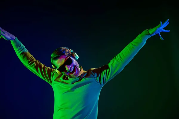 Foto de chico joven impresionado danza desgaste auriculares gafas suéter aislado sobre fondo de color azul oscuro —  Fotos de Stock