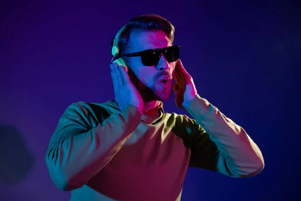 Φωτογραφία του funky αστείο νεαρός άνδρας φορούν ακουστικά sunglass clubber νυχτερινή ζωή απομονωμένη σε νέον φόντο — Φωτογραφία Αρχείου