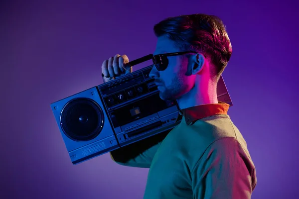 Profil sida foto av allvarliga cool ung man hålla hand boombox bära solfångarglas isolerad på neon bakgrund — Stockfoto