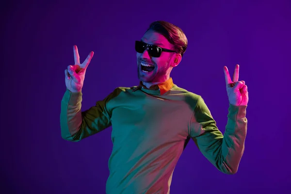 Foto retrato del hombre en el club nocturno mostrando gesto v-signo divertido aislado en el fondo de color púrpura — Foto de Stock