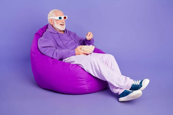 Full Size Profilseite Foto von gealterten Mann sitzen Sitzsack essen Popcorn-Uhr Kino 3D-Brille isoliert über violetten Farbhintergrund — Stockfoto