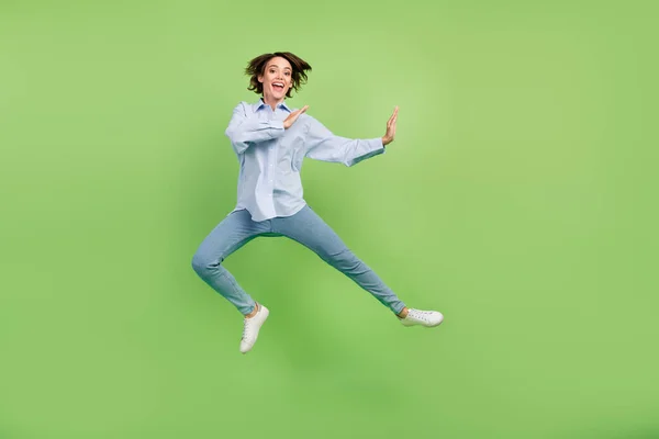 全长照片，照片上是快乐可爱的年轻快乐的女人跳起来的战斗机，兴奋的被绿色的背景隔开了 — 图库照片