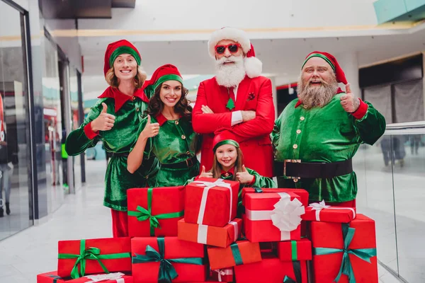 Portrait d'attrayant confiant joyeux joyeux amis funky elfes acheter des boîtes-cadeaux avènement montrant pouce au centre commercial à l'intérieur — Photo