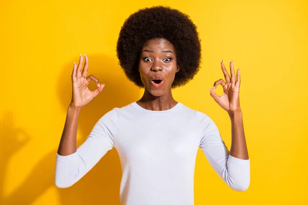 Foto von erstaunt wellige Frisur dunkle Haut Person offenen Mund Finger zeigen okey Symbol isoliert auf gelbem Hintergrund — Stockfoto