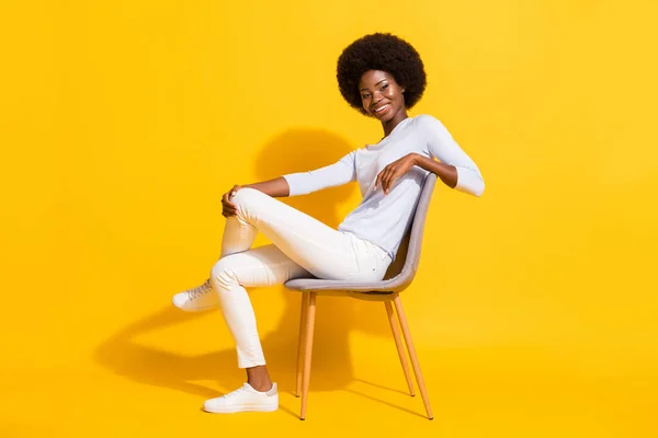 Full body profile portrait of adorable dark skin girl sit toothy smile look camera isolated on yellow color background — Stock Photo, Image