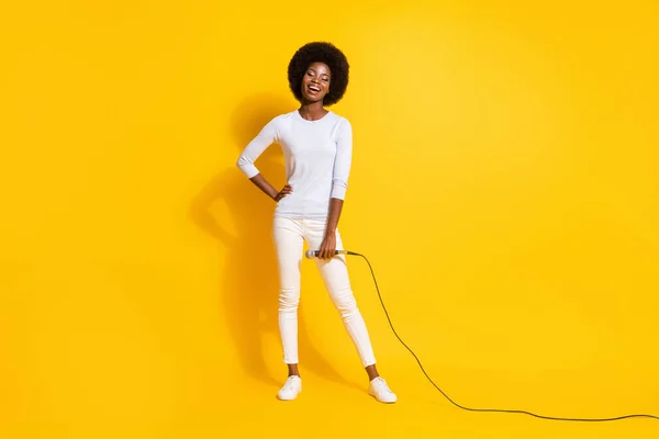 Full size photo of optimistic nice short hair lady stand with mic wear white pullover trousers sneakers isolated on yellow background — Stock Photo, Image