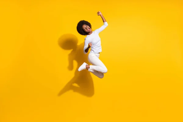 Foto de tamaño completo de la feliz mujer de piel oscura saltar levantar puños ganador aislado en el fondo de color amarillo brillante —  Fotos de Stock