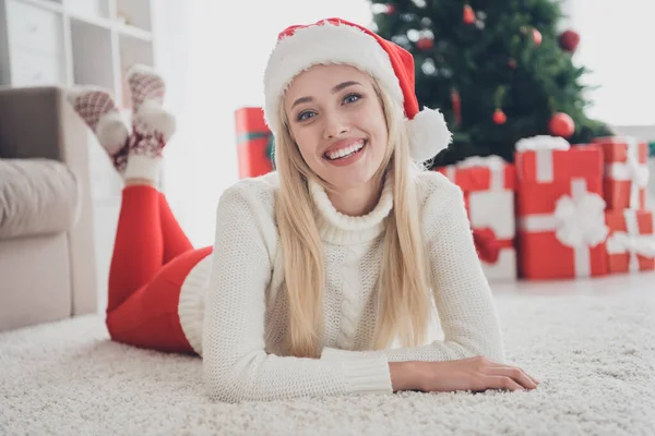Neşeli genç kızın tam boy fotoğrafı mutlu pozitif gülümseme yerde yatarken Noel Baba şapkası giyin kapalı yerde kış mevsimi atmosferi — Stok fotoğraf
