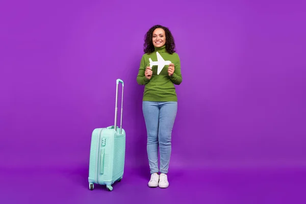 Fotografie sladké atraktivní afro žena nosí zelený rolák drží papír rovina zavazadla usmívá izolované fialové barvy pozadí — Stock fotografie