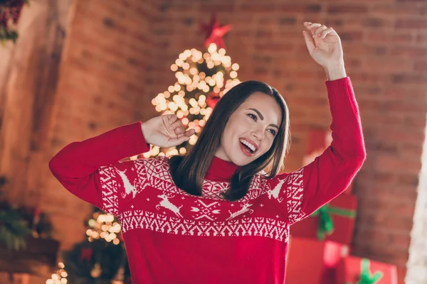 Фото блискучої позитивної леді в червоній пуловері, що посміхається насолоджуючись різдвяним духом, танцює в приміщенні домашньої кімнати будинку — стокове фото