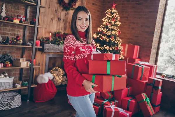 빨간 스웨터를 입고 새해 나무 아래 선물을 놓고 실내에서 미소짓고 있는 아름다운 한 젊은 여성의 사진 — 스톡 사진
