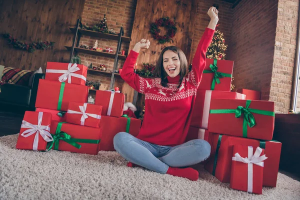 Fotografie okouzlující atraktivní mladá dáma nosit červený svetr usmívající se rostoucí pěsti vánoční dárky vnitřní dům domácí pokoj — Stock fotografie