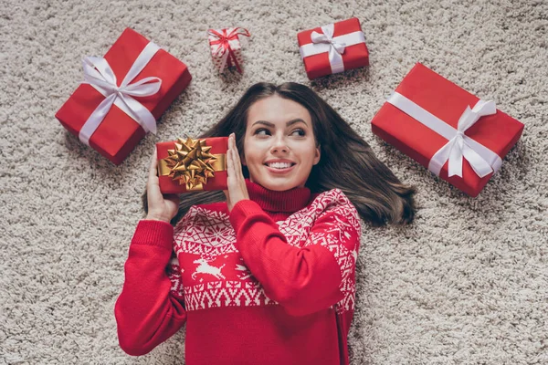 Çekici, rüya gibi genç bir kadının kırmızı kazak giyip ev içinde gülümseyen yeni yıl hediyelerini dinlemesi. — Stok fotoğraf