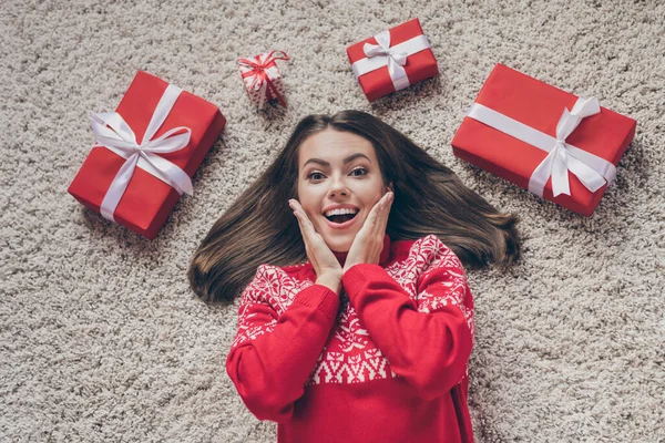 Foto de la joven atractiva impresionada usar jersey rojo brazos sonrientes manos mejillas pómulos regalos de Navidad interior casa habitación —  Fotos de Stock