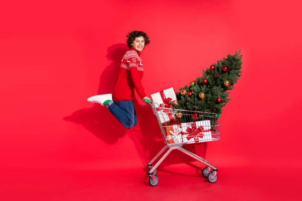 顾客男孩提着购物车买圣诞礼物的照片跳起来穿鹿饰衫孤立的红色背景 — 图库照片