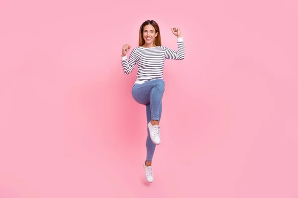Foto de longitud completa de maduro fresco pelo marrón señora salto usar camisa jeans zapatillas aisladas sobre fondo rosa —  Fotos de Stock