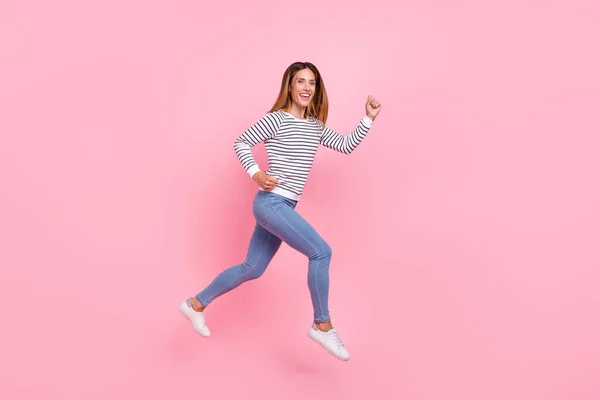 Повнометражний профіль фотографія зрілої красивої коричневої волосся леді біжить носити сорочки джинси кросівки ізольовані на рожевому фоні — стокове фото
