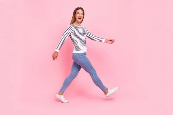 Foto de divertida joven brillante vestida a rayas suéter caminando sonriente aislado color rosa fondo —  Fotos de Stock