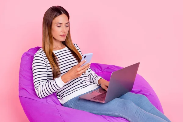 Foto de senhora madura muito ocupada usar camisola listrada sorrindo sentado beanbag trabalhando gadgets modernos isolado cor de rosa fundo — Fotografia de Stock