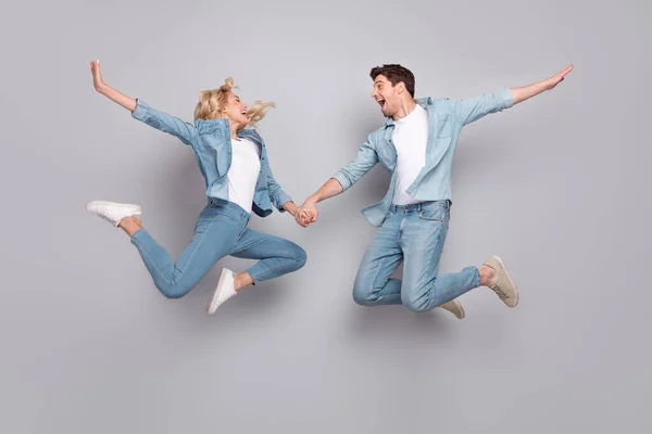 Foto de pareja amante inspirado salto agarrarse de la mano desgaste casual jeans traje aislado color gris fondo — Foto de Stock