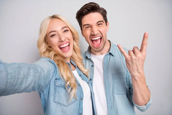 Foto de jovem casal animado feliz sorriso positivo mostrar dedos chifres de rocha sinal tomar selfie isolado sobre fundo de cor cinza — Fotografia de Stock