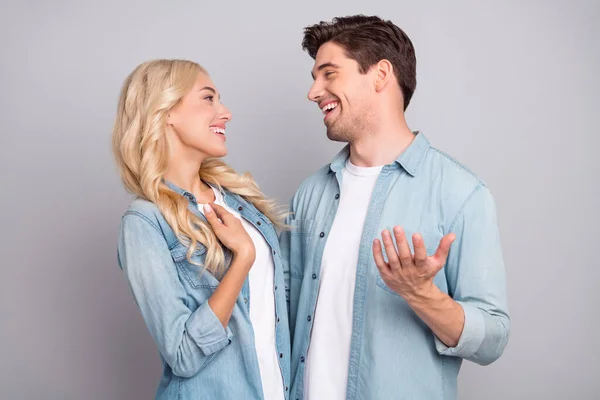 Foto de bonito casal muito jovem vestido jeans camisas sorrindo abraçando falando isolado fundo de cor cinza — Fotografia de Stock