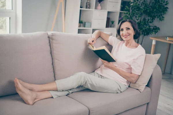 Фотография в полный рост пожилой брюнетки симпатичная дама сидит на диване читать носить розовые брюки футболки дома в одиночестве — стоковое фото