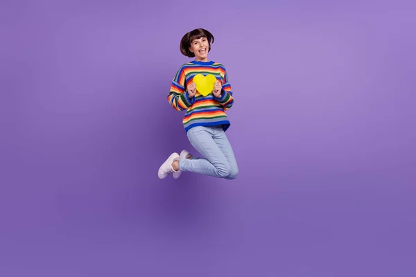 Foto inspirované flirtující dáma skok držet srdce karty nosit pruhované svetr džíny boty izolované fialové barvy pozadí — Stock fotografie