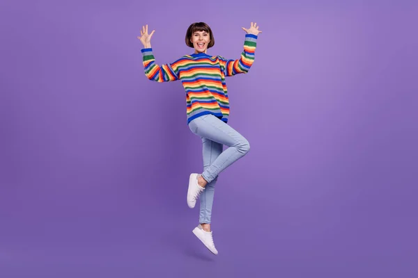 Foto de alegre sonho senhora salto levantar braços desgaste listrado camisola jeans sapatos isolado cor violeta fundo — Fotografia de Stock