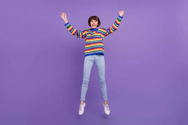 Foto av glad söt dam hoppa njuta av helgen slitage randig pullover jeans skor isolerad violett färg bakgrund — Stockfoto