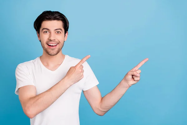 Foto de cara feliz engraçado indicar dedos indicador espaço vazio venda banner desgaste branco t-shirt isolado azul cor fundo — Fotografia de Stock